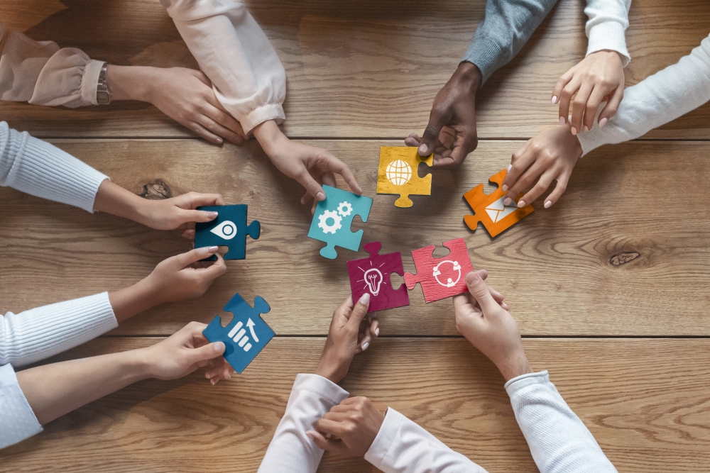 People with their hands on a table each holding a piece of a puzzle